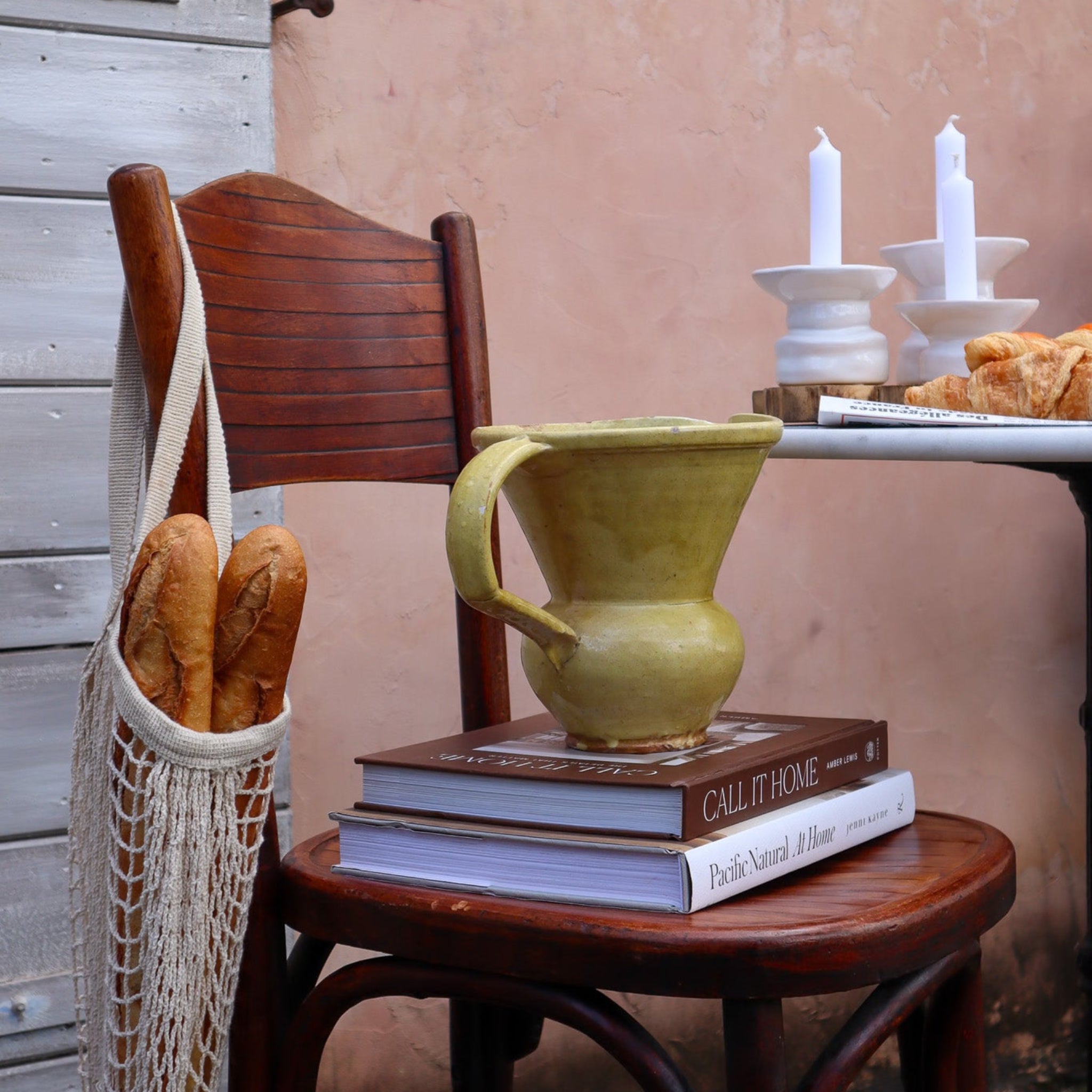 Green ceramic mug on books with a wooden chair and bread in the background