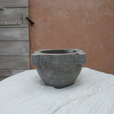 A gray stone mortar and pestle set on a white fabric-covered surface, with a rustic terracotta wall and weathered wooden door in the background.